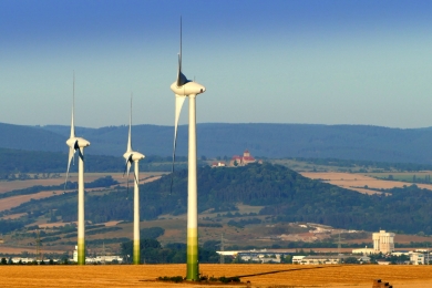 Drei Windräder seitlich, in der Bildmitte dahinter die Wachsenburg, blauer Himmel
